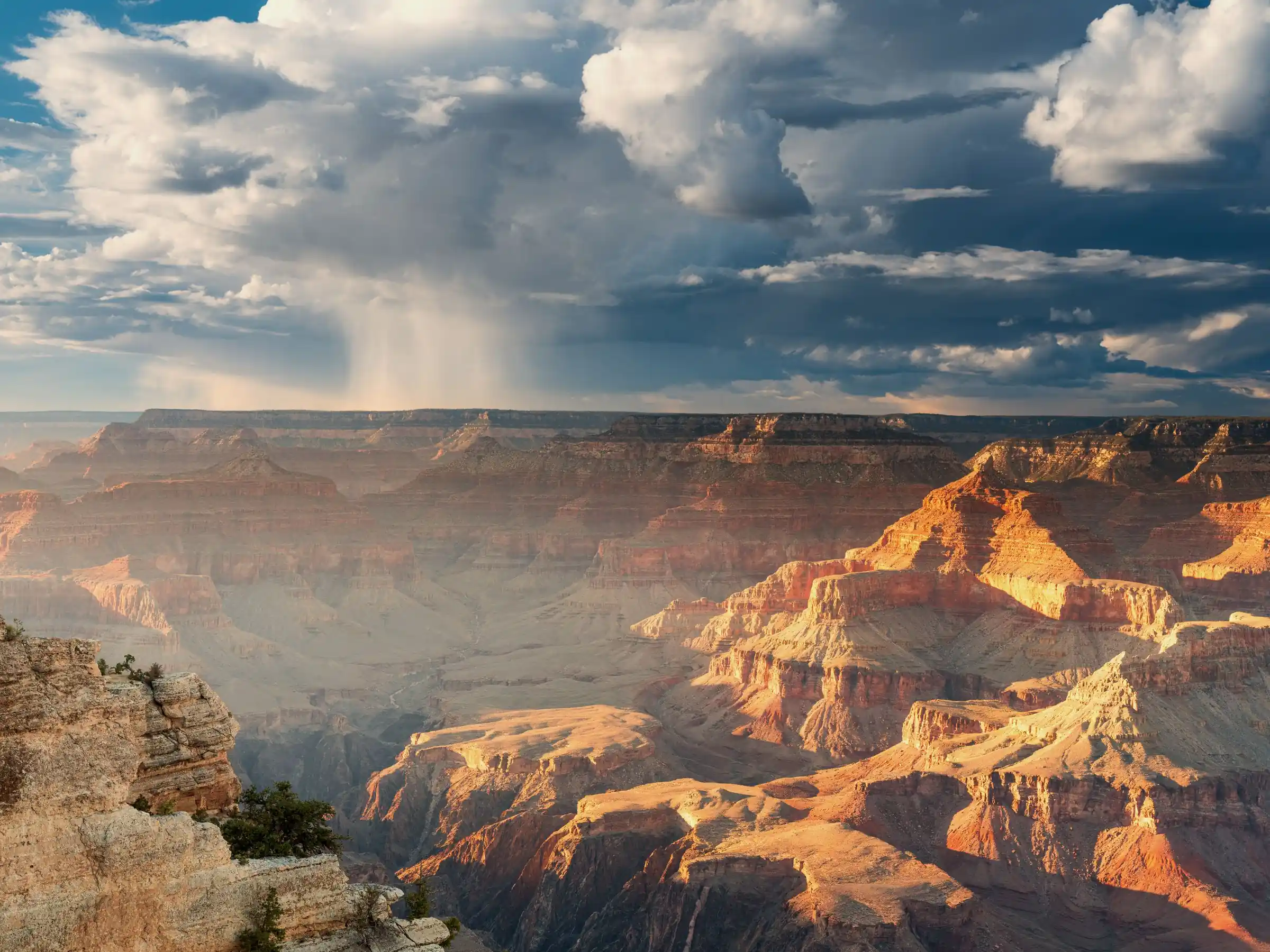 Rain falling over the Grand Canyon, layered red rock receding into the haze