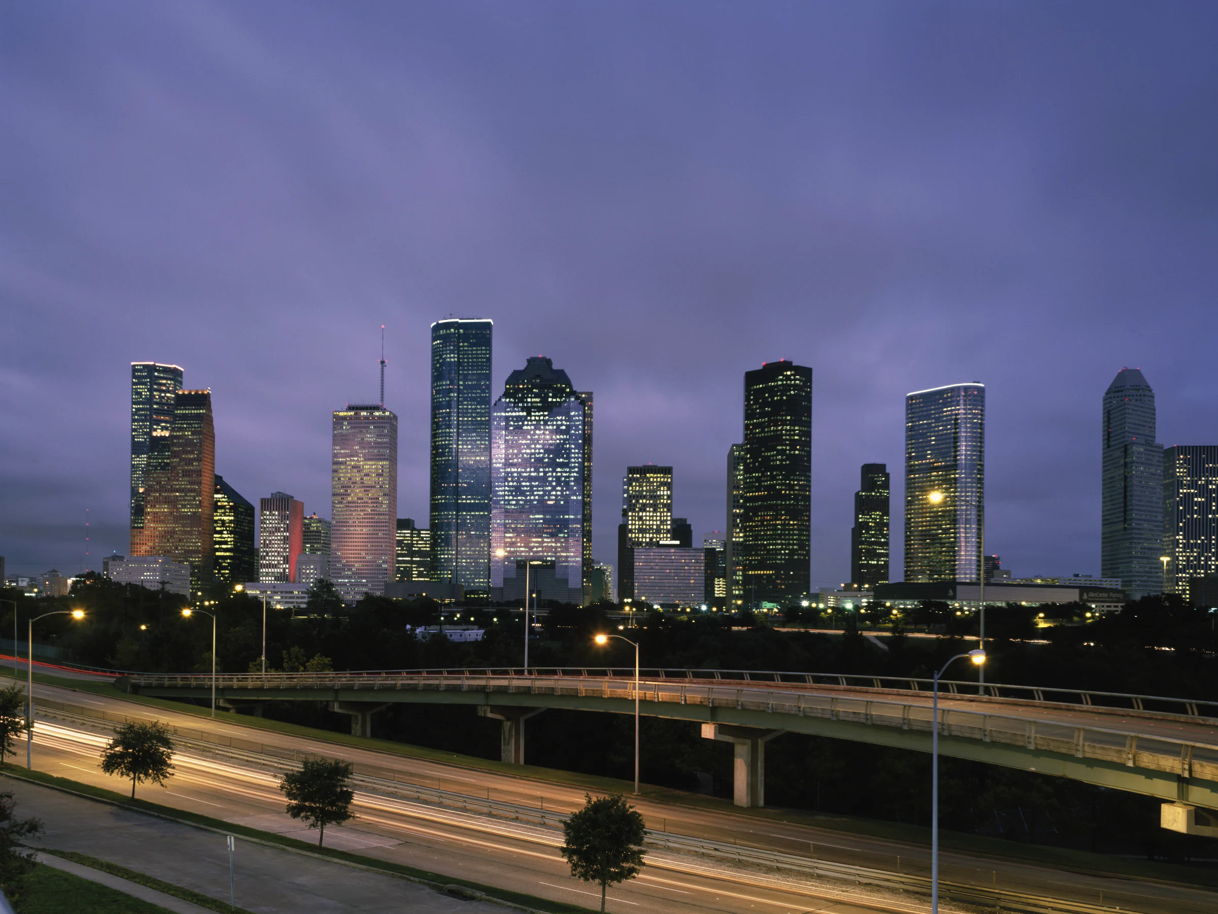The downtown Houston skyline at dusk, glass towers over the freeway lights